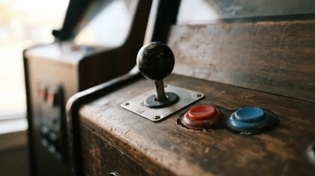 A close-up, low-angle shot of a classic arcade joystick, its well-worn red and blue buttons illuminated by warm