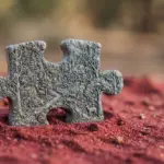 A stone puzzle piece carved with a forest scene sits upright in red sand