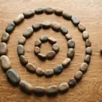 A close-up, top-down view of smooth, naturally colored river stones arranged in a gentle, imperfect spiral on a warm